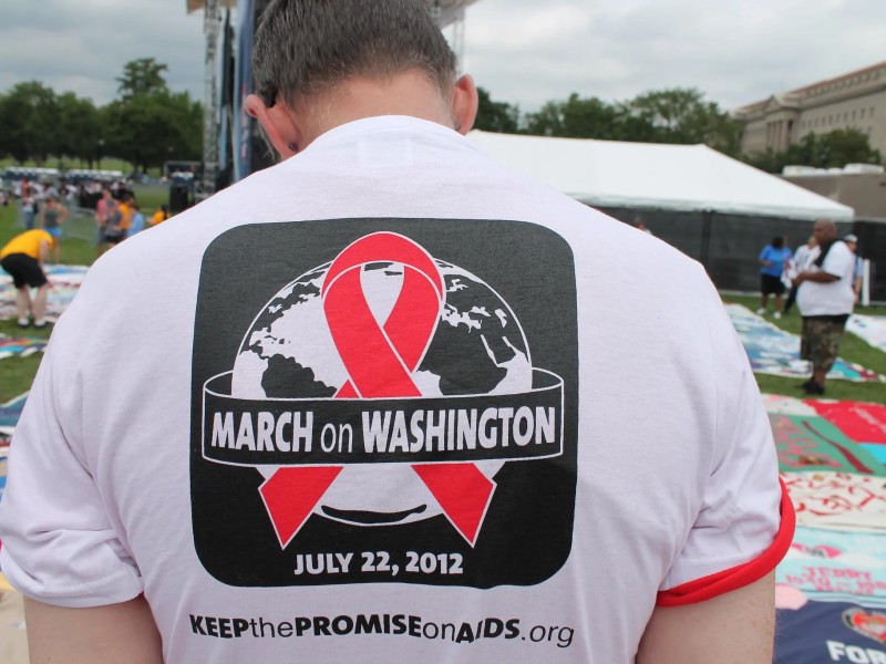 The back of a white man wearing a March on Washington tee and standing at the AIDS Quilt on the Mall in Washington DC. Photo by Elvert Barnes via Flickr