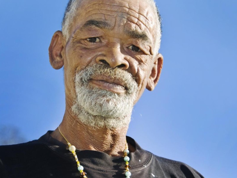 Black elder in black tee looks at camera with blue sky behind him.